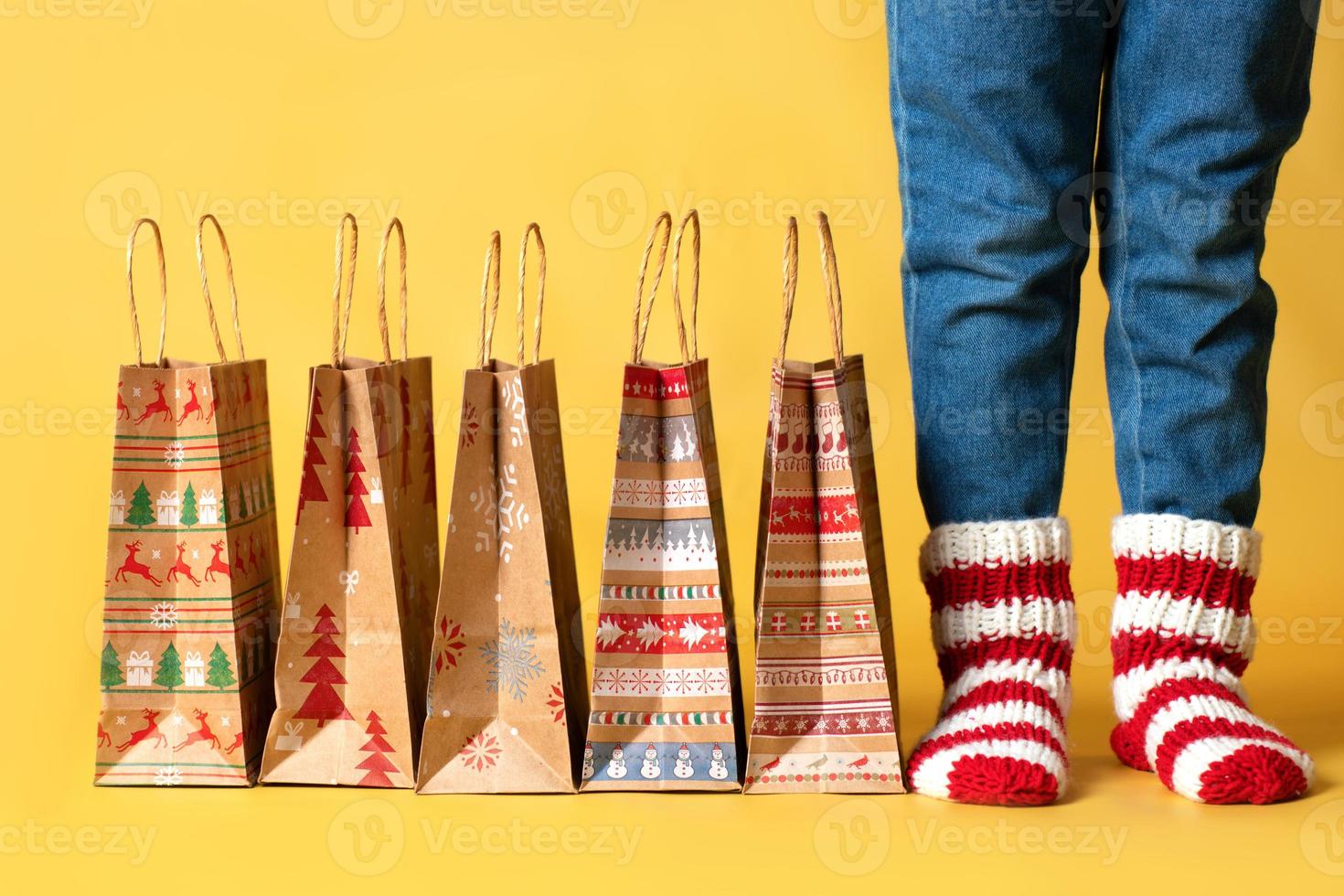 livraison de cadeaux de noël shopping sacs en papier kraft cadeaux et enfant en chaussettes tricotées fond jaune isolé surprise pour les enfants photo