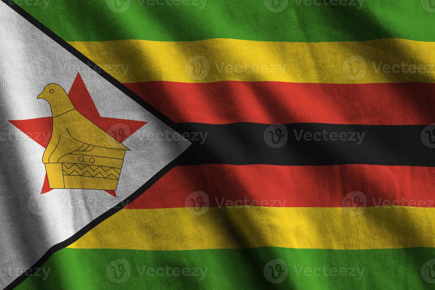 drapeau du zimbabwe avec de grands plis agitant de près sous la lumière du studio à l'intérieur. les symboles et couleurs officiels de la bannière photo