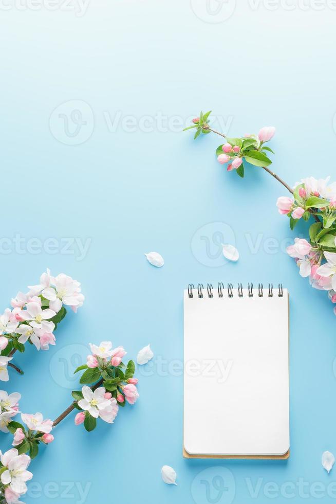 sakura de printemps en fleurs sur fond bleu avec espace bloc-notes pour un message d'accueil. le concept du printemps et de la fête des mères. belles fleurs de cerisier roses délicates au printemps photo