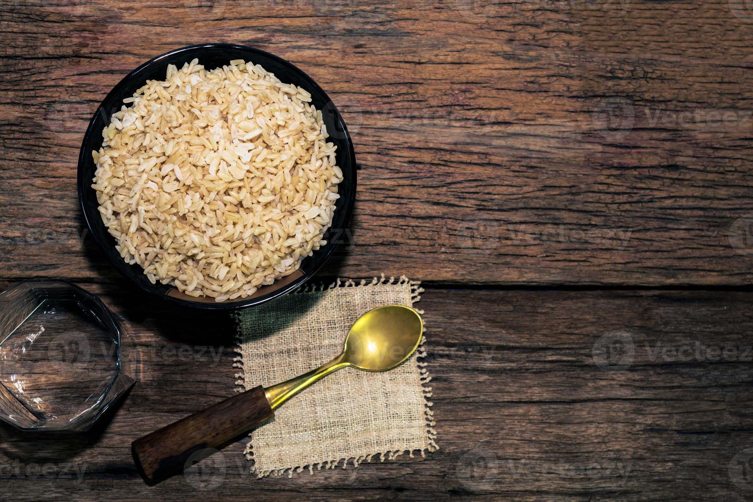 Le riz brun dans un bol noir a une cuillère isolée sur une table en bois photo