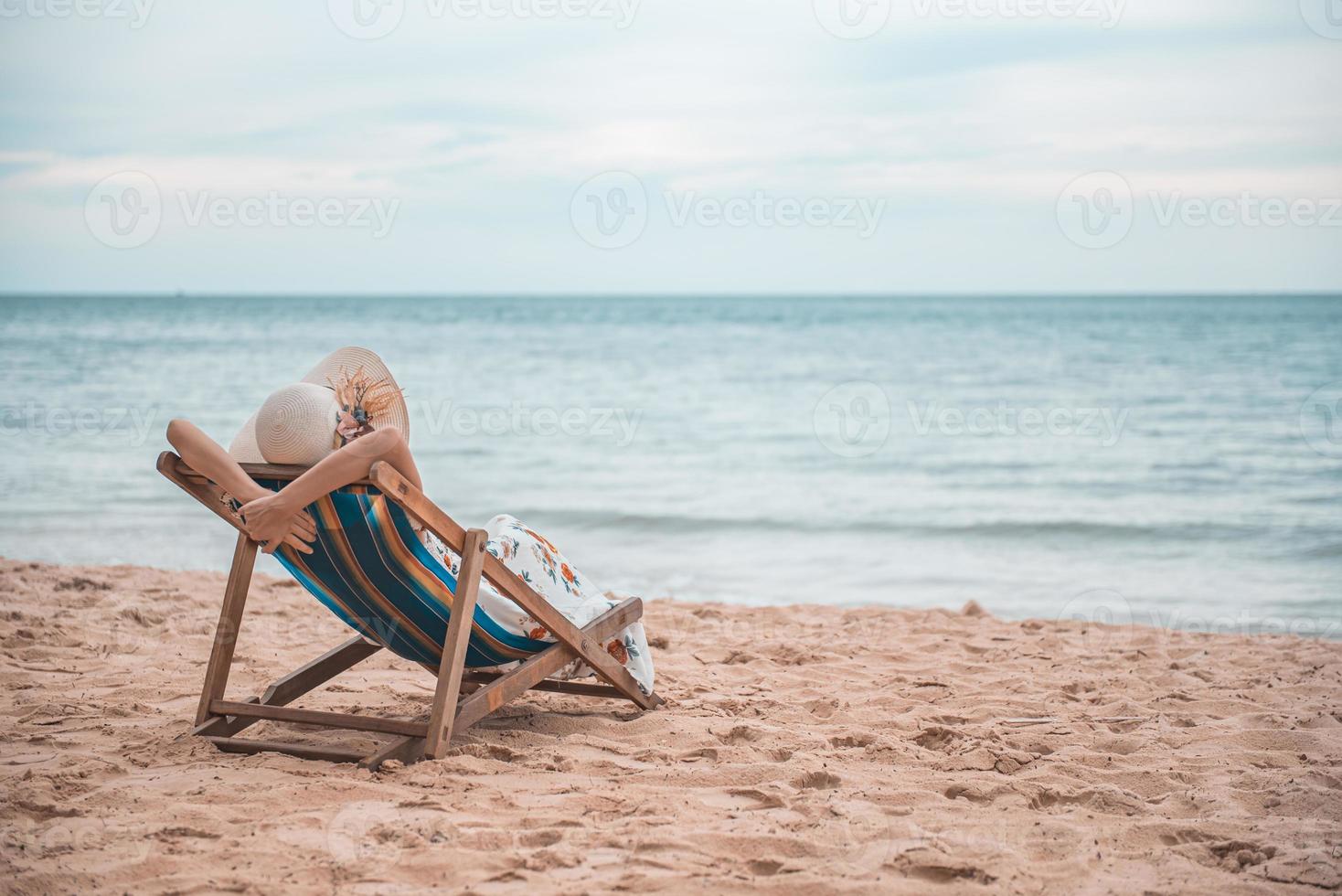 belle jeune femme asiatique avec un chapeau bras vers le haut relaxant sur une chaise de plage, concept de vacances d'été heureuses. photo