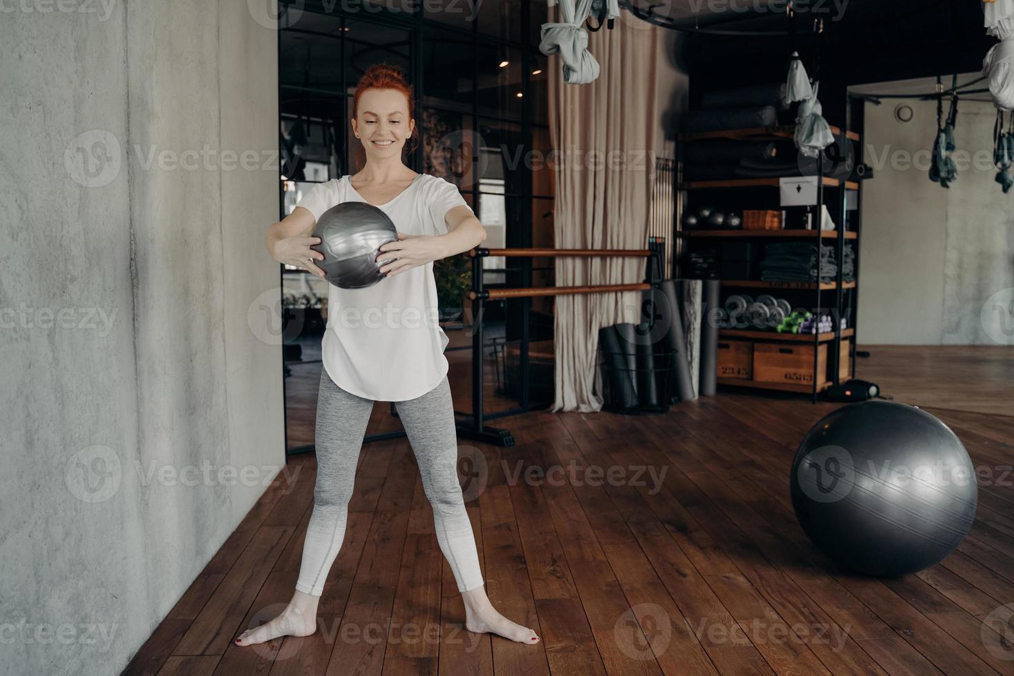 jeune femme en forme aux cheveux rouges profitant d'une séance d'entraînement à la barre avec un petit ballon de fitness photo