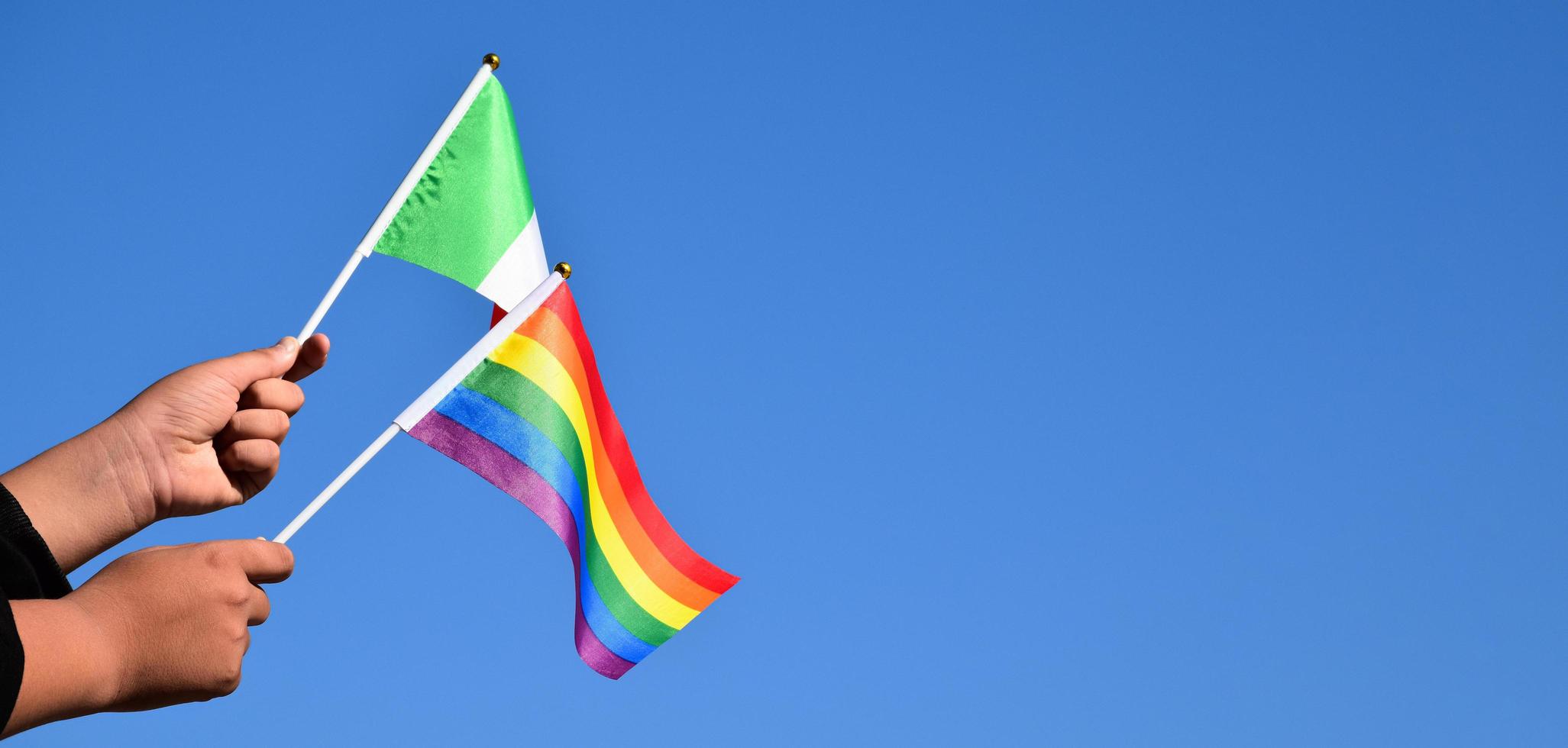 drapeau italien et drapeau arc-en-ciel, symbole lgbt, tenant dans les mains, fond bleu ciel, concept pour la célébration lgbt en italie et dans le monde en mois de fierté, juin, mise au point douce et sélective, espace de copie. photo