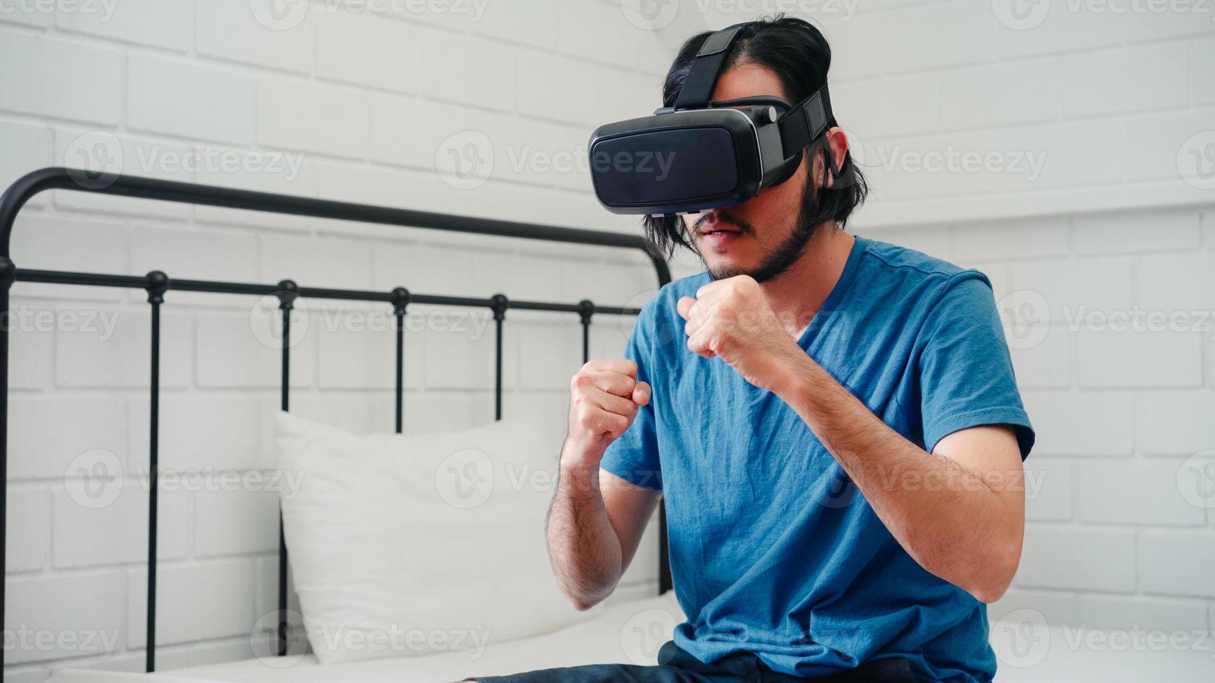 jeune homme asiatique utilisant des lunettes simulateur de réalité virtuelle jouant à un jeu de boxe dans la chambre, un homme japonais se sentant heureux en utilisant le temps de détente allongé sur le lit à la maison. les jeux pour adolescents se détendent à la maison. photo