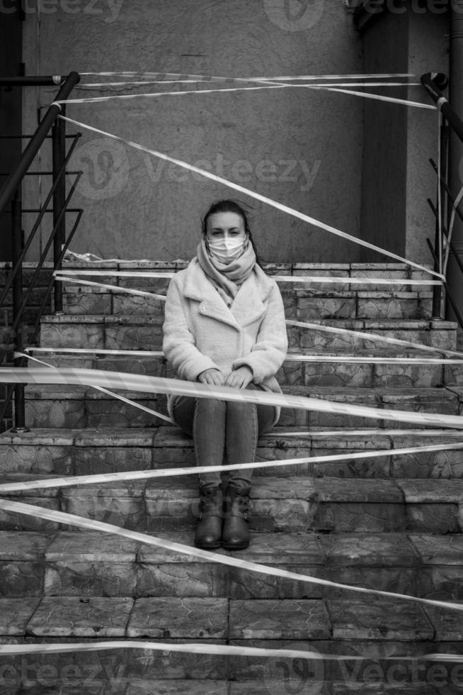 photo d'une fille dans un masque. assis dans la rue avec des bandes d'avertissement de danger.