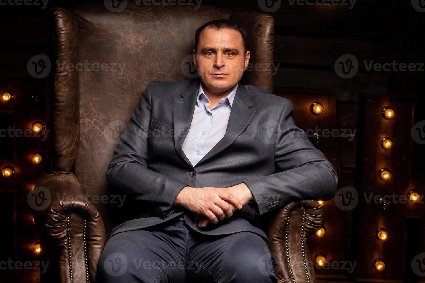 bel homme d'affaires en costume regarde la caméra sur une chaise en cuir. photo
