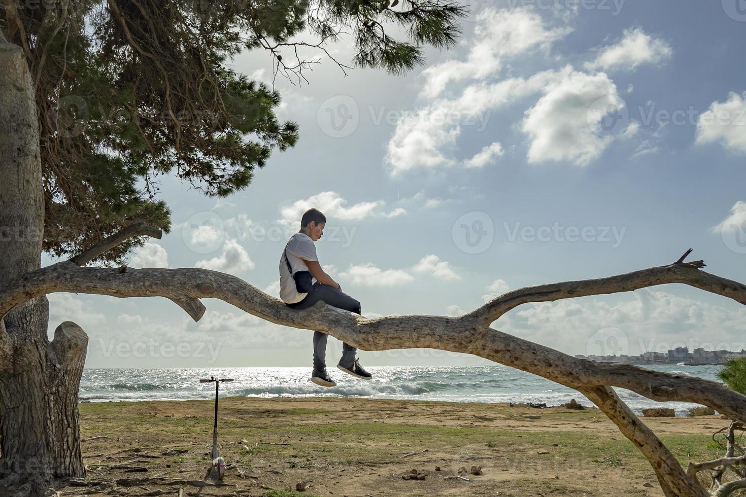 adolescent grimpant à un arbre contre le ciel bleu devant la mer photo