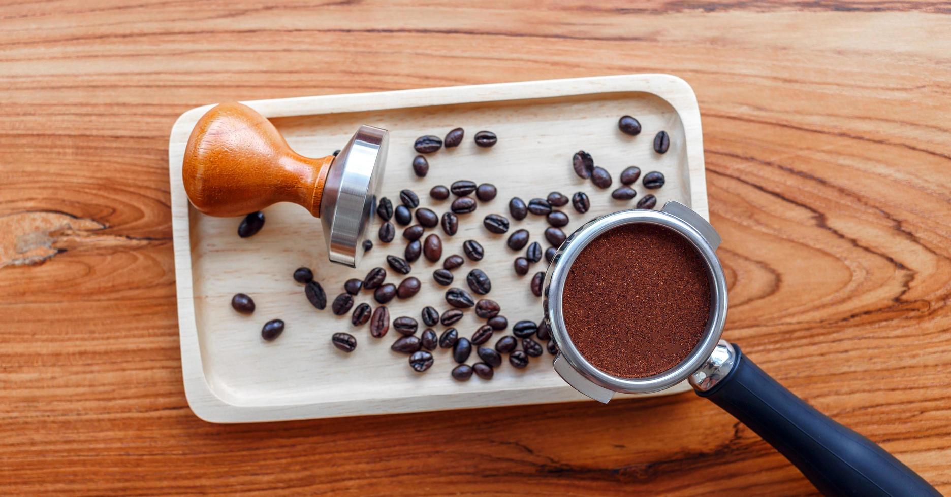 équipement d'outil de café barista inviolable et café tempéré dans des grains de café torréfiés de porte-filtre sur une table en bois photo