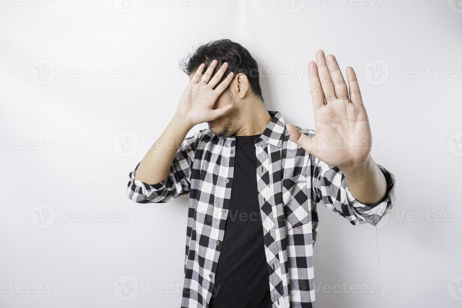 jeune homme asiatique effrayé isolé sur fond blanc, a l'air déprimé, le visage couvert de doigts effrayés et nerveux. photo