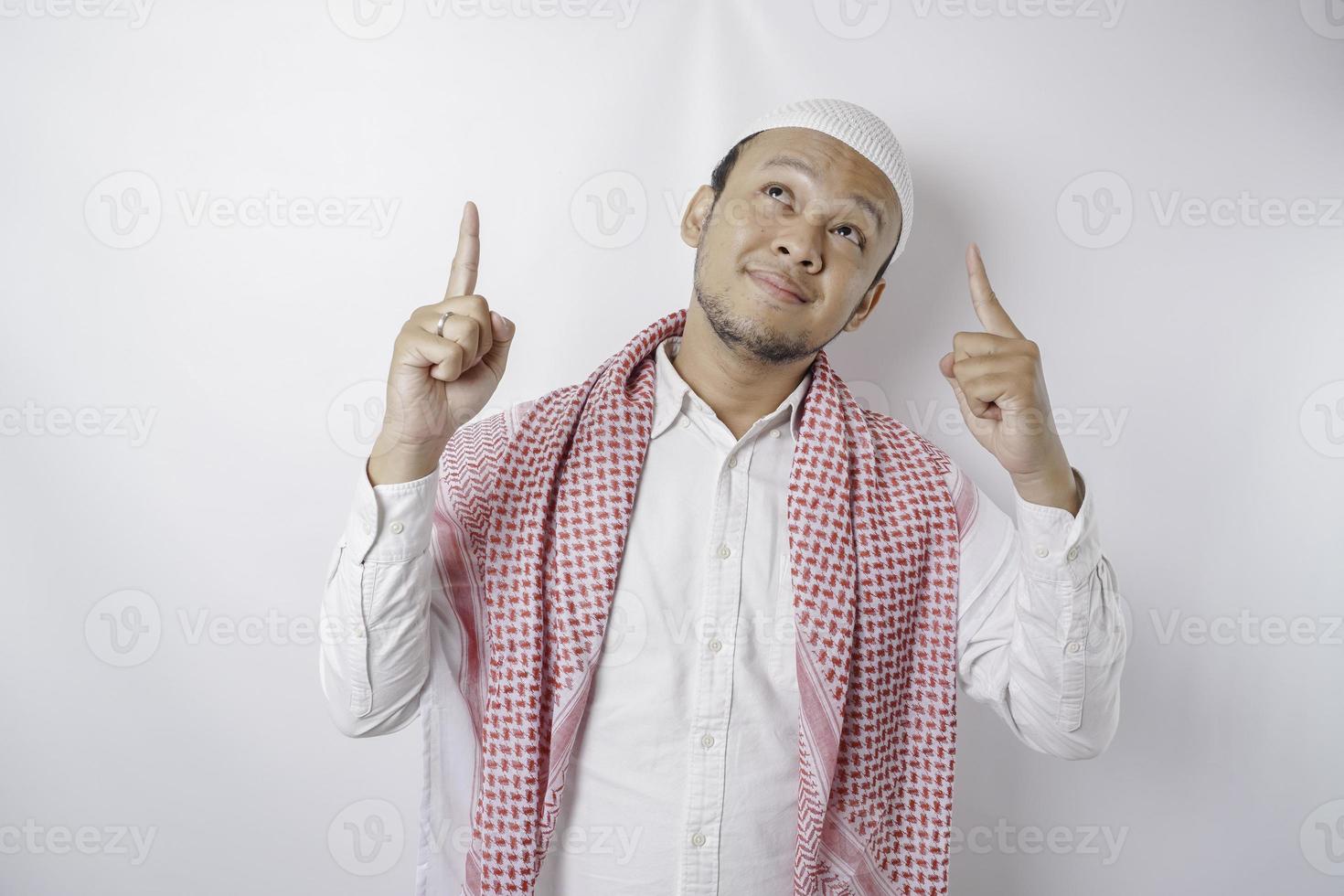 homme musulman asiatique souriant pointant vers l'espace de copie au-dessus de lui, isolé sur fond blanc photo