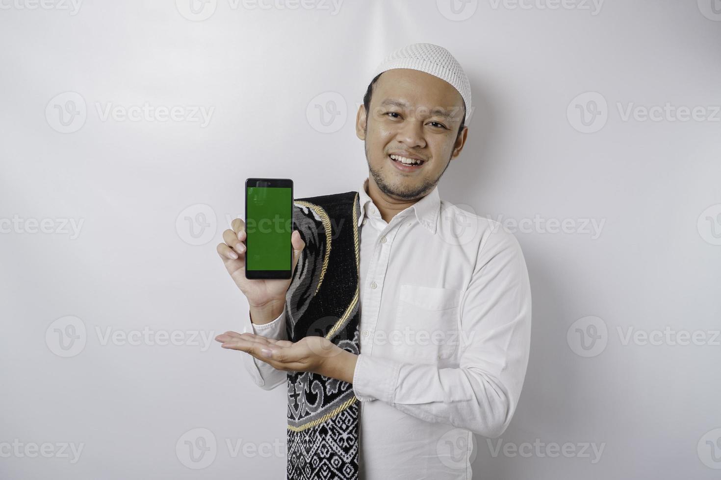 un portrait d'un homme musulman asiatique heureux souriant tout en montrant l'espace de copie sur son téléphone, isolé sur fond blanc photo