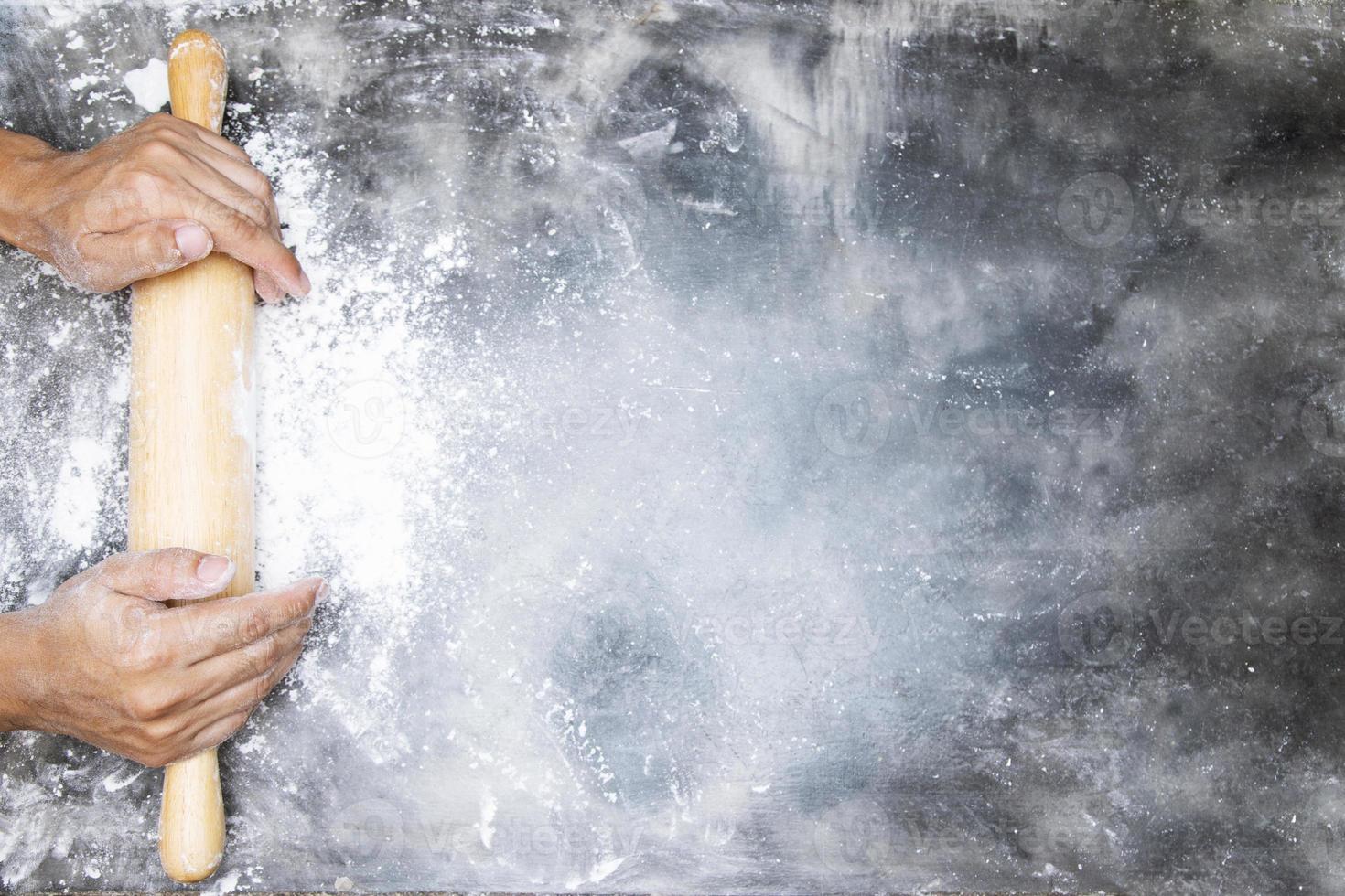 les jeunes mains gardent le rouleau à pâtisserie en purée avec de la farine de battage sur le tableau noir foncé, fond de boulangerie avec le rouleau à pâtisserie avec de la pâte. espace vide pour le texte. vue de dessus photo