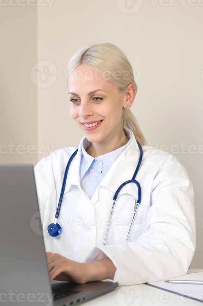 technologie moderne pour les soins de santé. bannière verticale avec une femme médecin souriante s'asseoir au bureau utiliser un ordinateur portable regarder un webinaire de formation professionnelle en ligne gérer un document médical électronique. photo