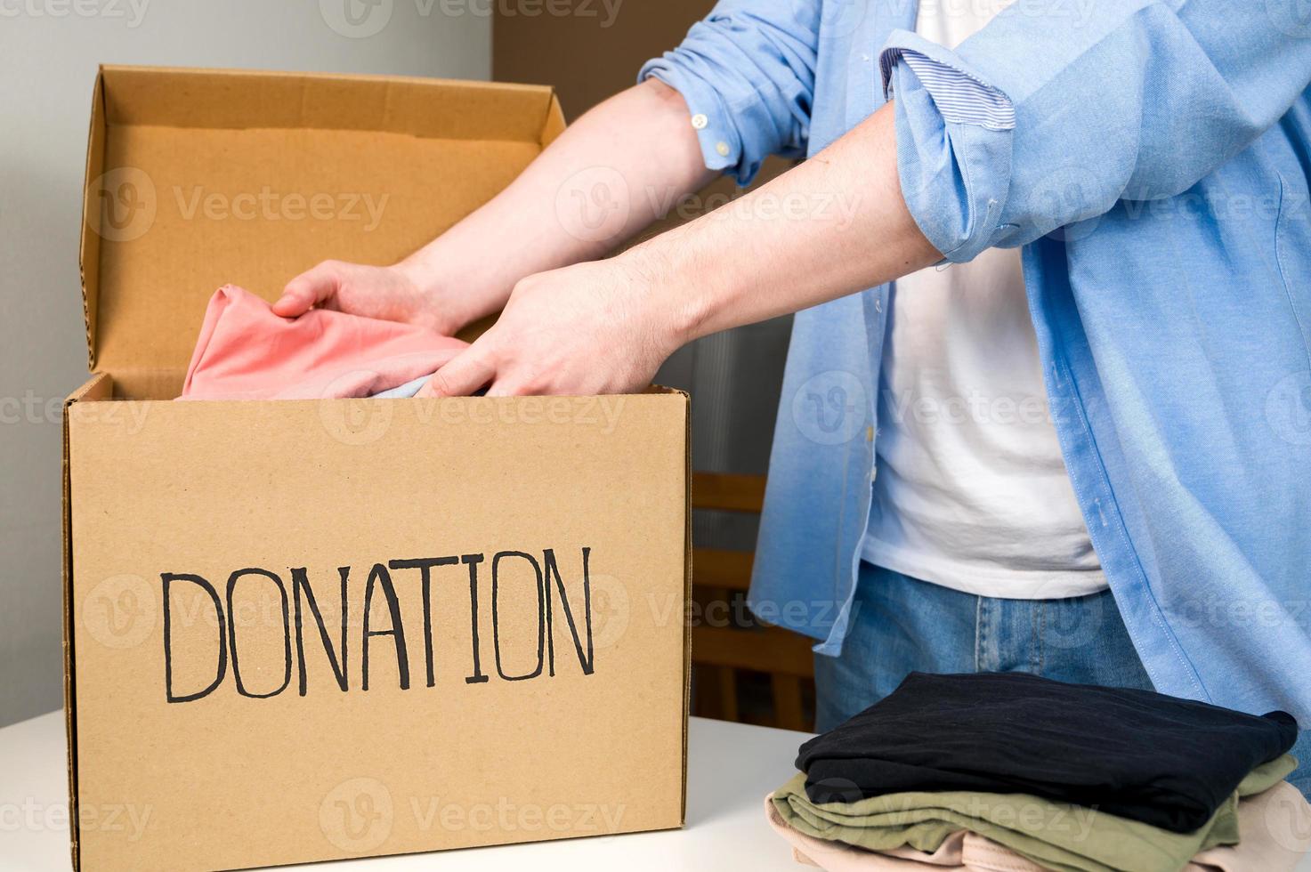 un volontaire masculin met des vêtements dans une boîte de dons. boîte en carton avec des vêtements pour la charité. aider les pauvres.partager l'activité sociale. photo