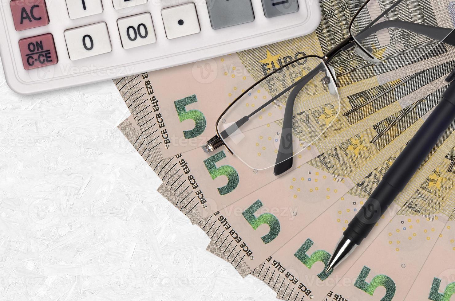 Fan de billets de 5 euros et calculatrice avec lunettes et stylo. prêt aux entreprises ou concept de saison de paiement des impôts photo