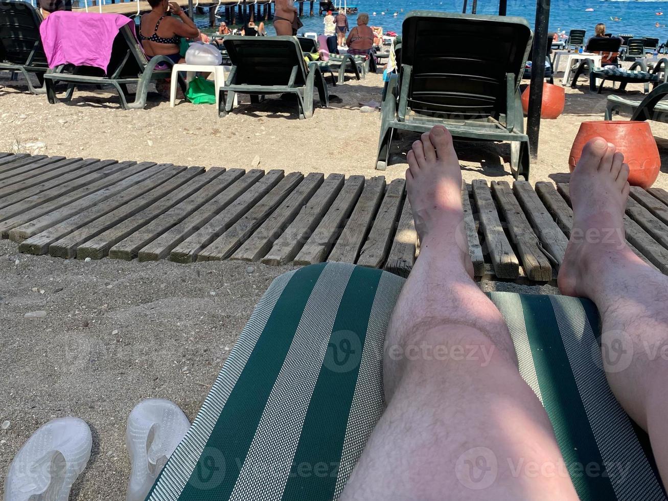 orientation horizontale des pieds mâles sur un transat donnant sur une piscine à débordement vers l'océan, avec un espace réservé au texte photo