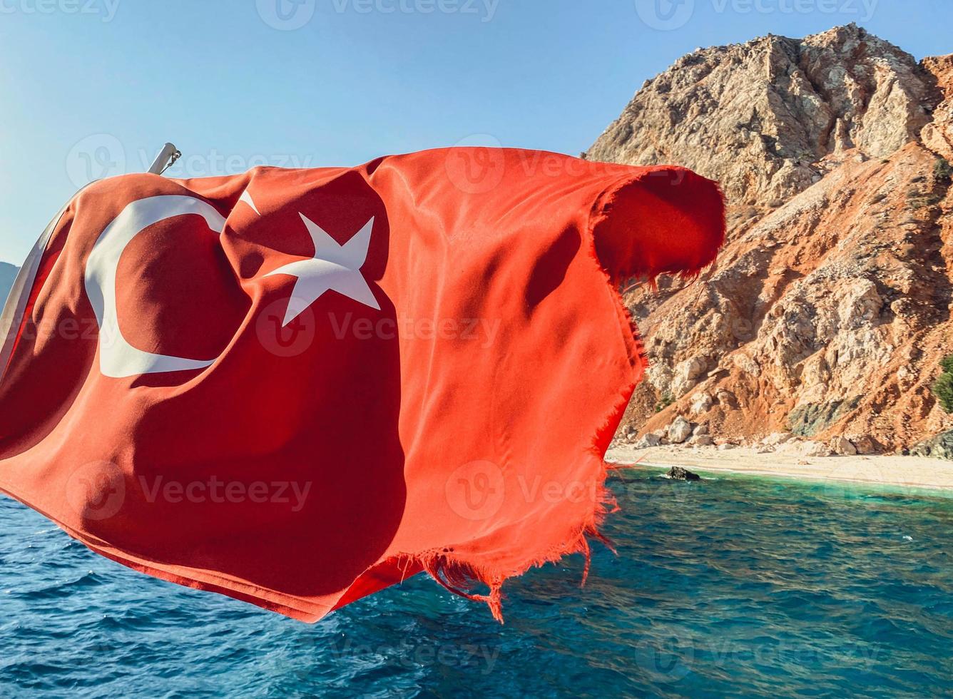 rocher au centre de la mer. une eau bleue avec de l'écume bouillonnante avec une grande et haute montagne au centre. le drapeau turc flotte au vent photo