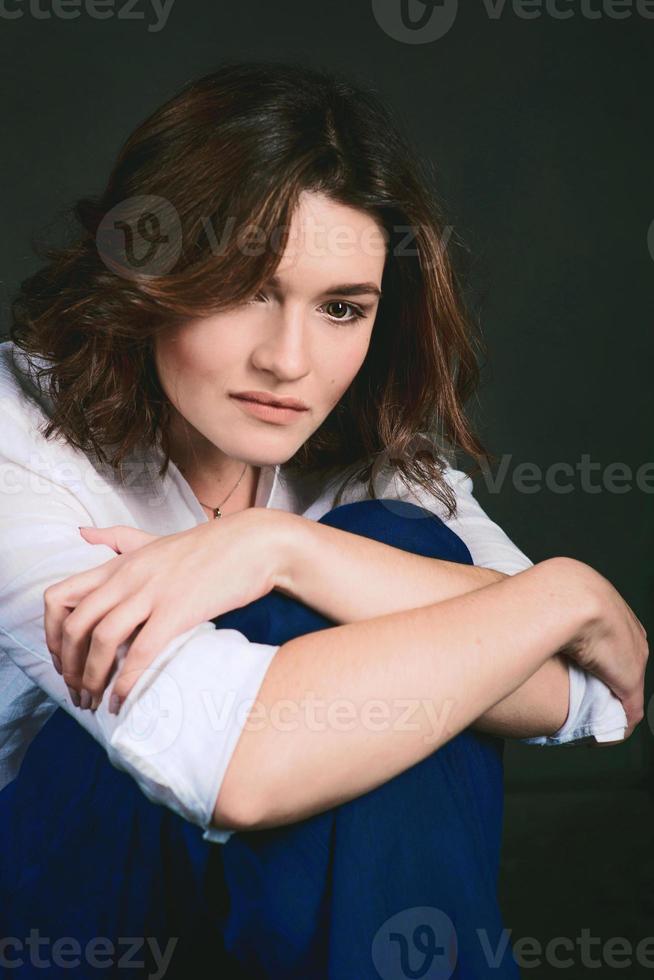 portrait d'une jeune et belle actrice triste aux cheveux bruns courts en chemise blanche et pantalon bleu en studio photo