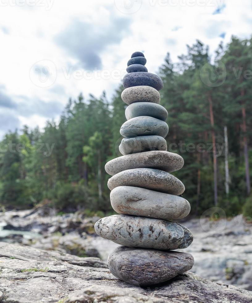 une pyramide de pierres nues empilées les unes sur les autres. pierres empilées en forme de pyramide sur la berge sur fond de montagnes comme équilibre et équilibre dans la nature, zen, bouddhisme. photo