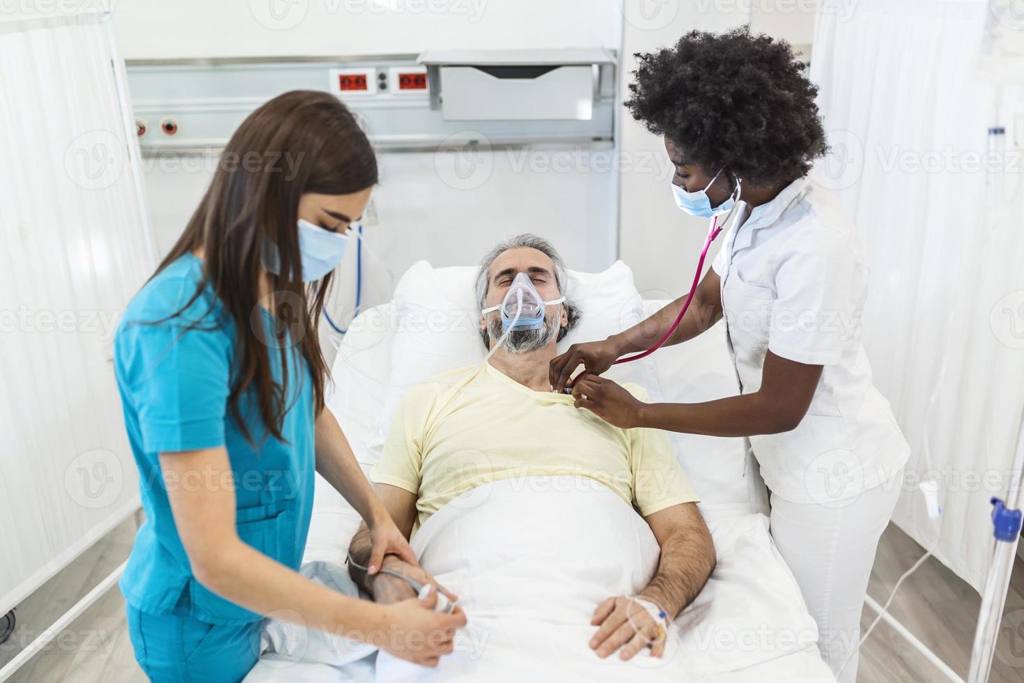 les médecins avec des masques de protection examinent le patient vieillissant infecté à l'hôpital. à l'hôpital, le patient âgé repose avec un masque à oxygène, allongé sur le lit. photo