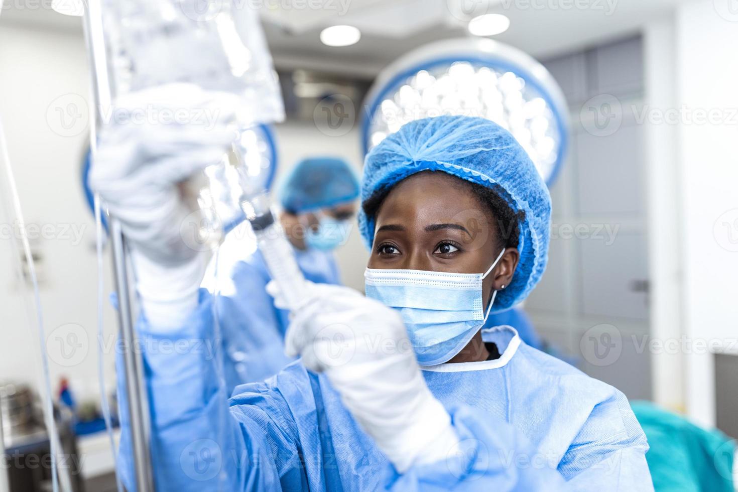 femme médecin afro-américaine dans la salle d'opération mettant des médicaments par voie intraveineuse - concepts de chirurgie photo