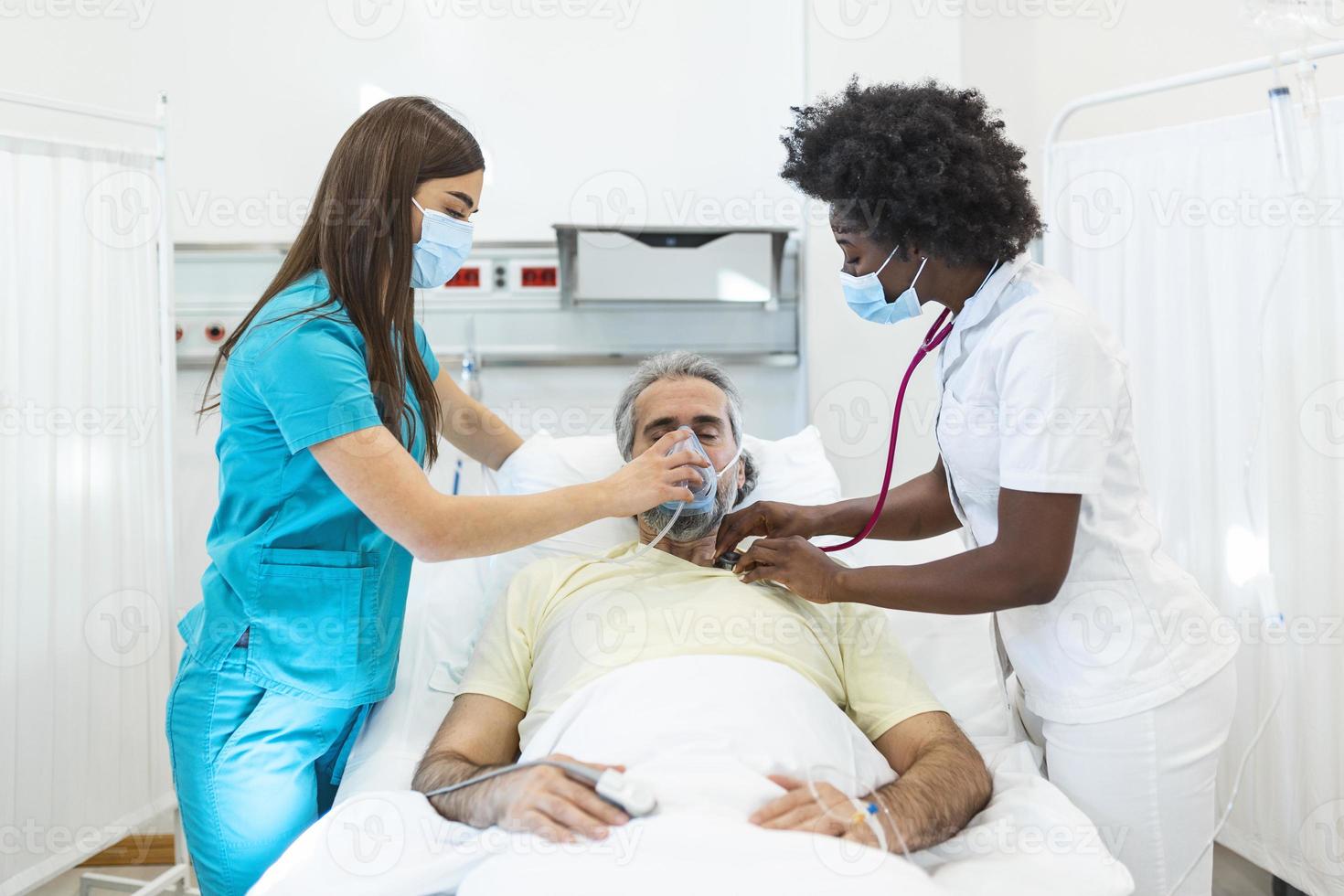 jeune médecin et infirmière portant un masque chirurgical vérifiant un patient âgé portant un masque à oxygène à pression positive pour aider à respirer dans un lit d'hôpital pendant la pandémie de covid-19 photo