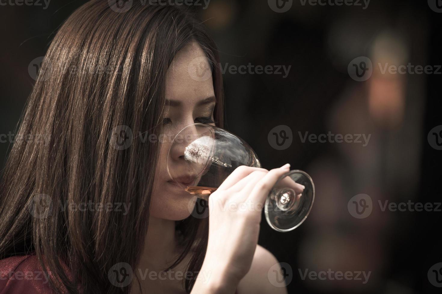 nouvel an, noël, célébrations de fête de nuit concept jeune femme asiatique heureuse tenant et buvant un verre d'alcool au bar de nuit ou à la discothèque. photo
