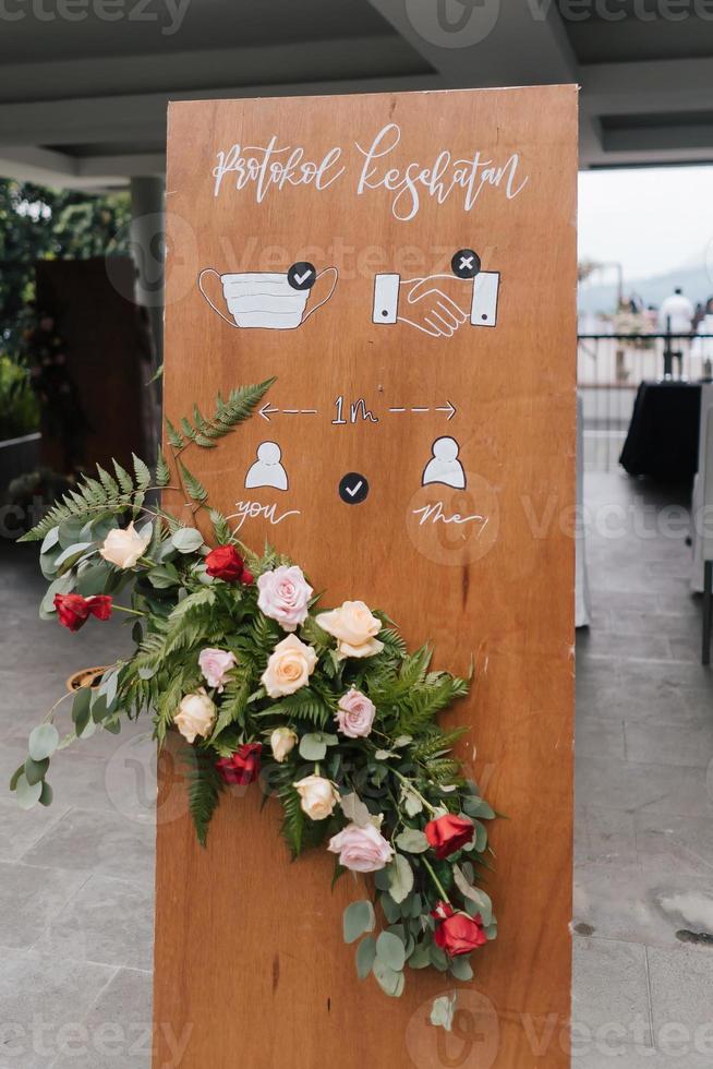 un panneau avant se traduit en indonésie par un protocole de santé, avec une décoration florale à l'entrée du mariage. photo