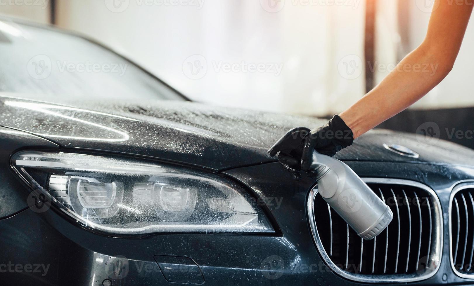 pulvériser le véhicule. une automobile noire moderne est nettoyée par une femme à l'intérieur d'une station de lavage de voiture photo