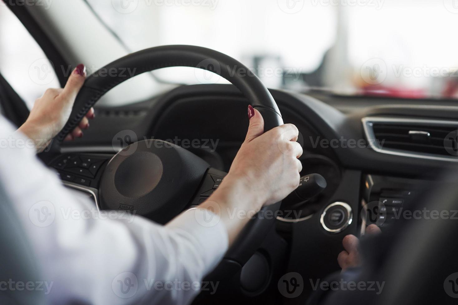 mains sur le volant. femme en tenue officielle essayant sa nouvelle voiture dans un salon automobile photo