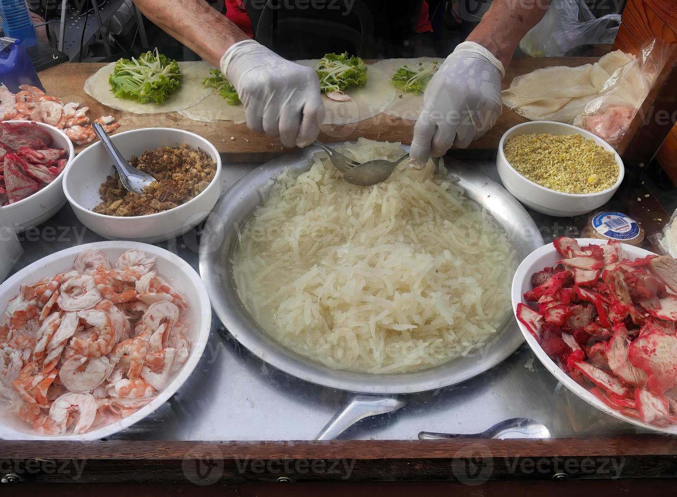 le vendeur met des gants dans la préparation d'un rouleau de printemps frais rempli de porc rouge, de crevettes, de germes de soja et de radis à emporter au client. menu appliqué servi sur le marché thaïlandais de l'alimentation de rue. photo