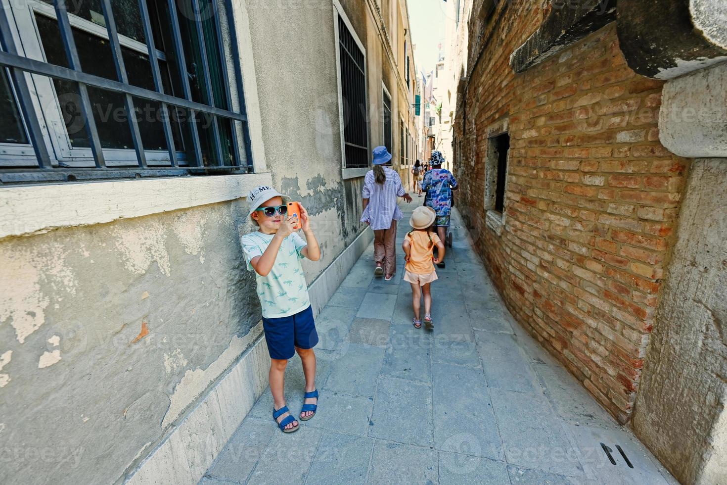 les enfants marchent dans les rues étroites en briques de venise, en italie. garçon touriste faisant une photo par téléphone.