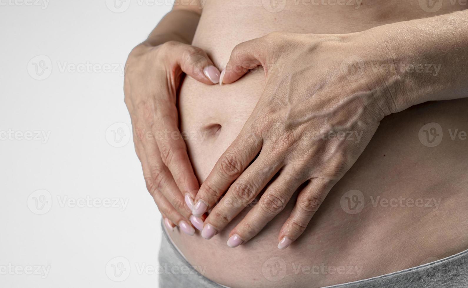 femme enceinte tient les mains sur le ventre sur un fond bleu. concept de grossesse, de maternité, de préparation et d'attente. gros plan, à l'intérieur. belle photo