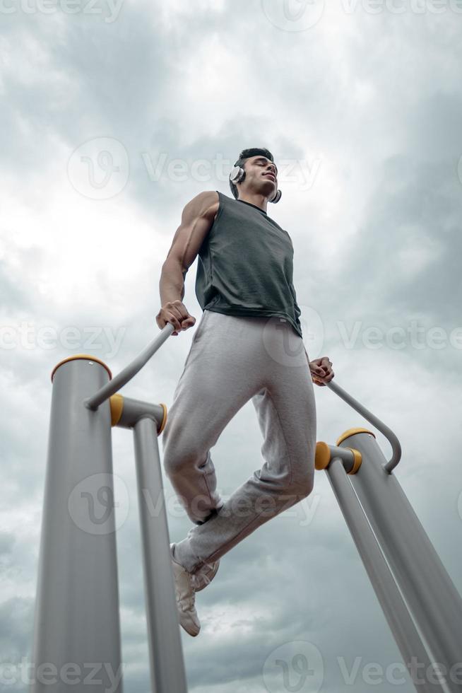 sportif travaillant sur l'équipement public sportif dans la salle de sport en plein air. un homme actif sportif dans un parc par temps nuageux. photo