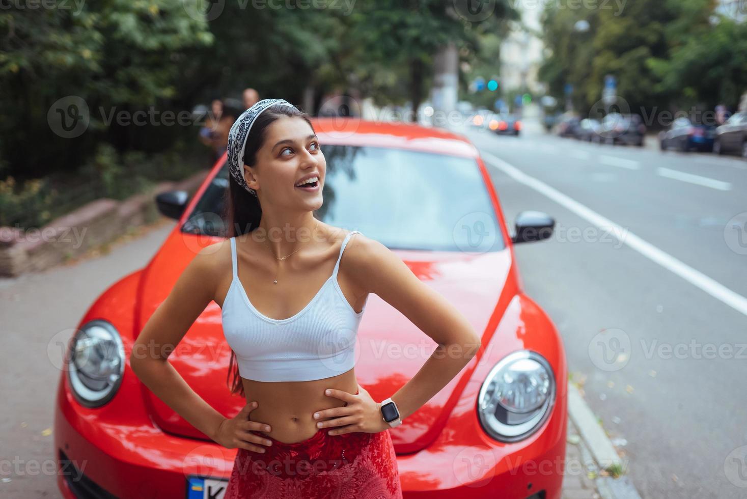 portrait d'une jolie femme caucasienne debout contre une nouvelle voiture rouge photo