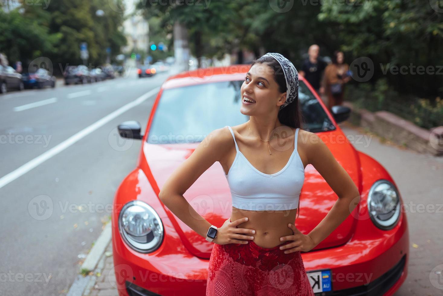 portrait d'une jolie femme caucasienne debout contre une nouvelle voiture rouge photo