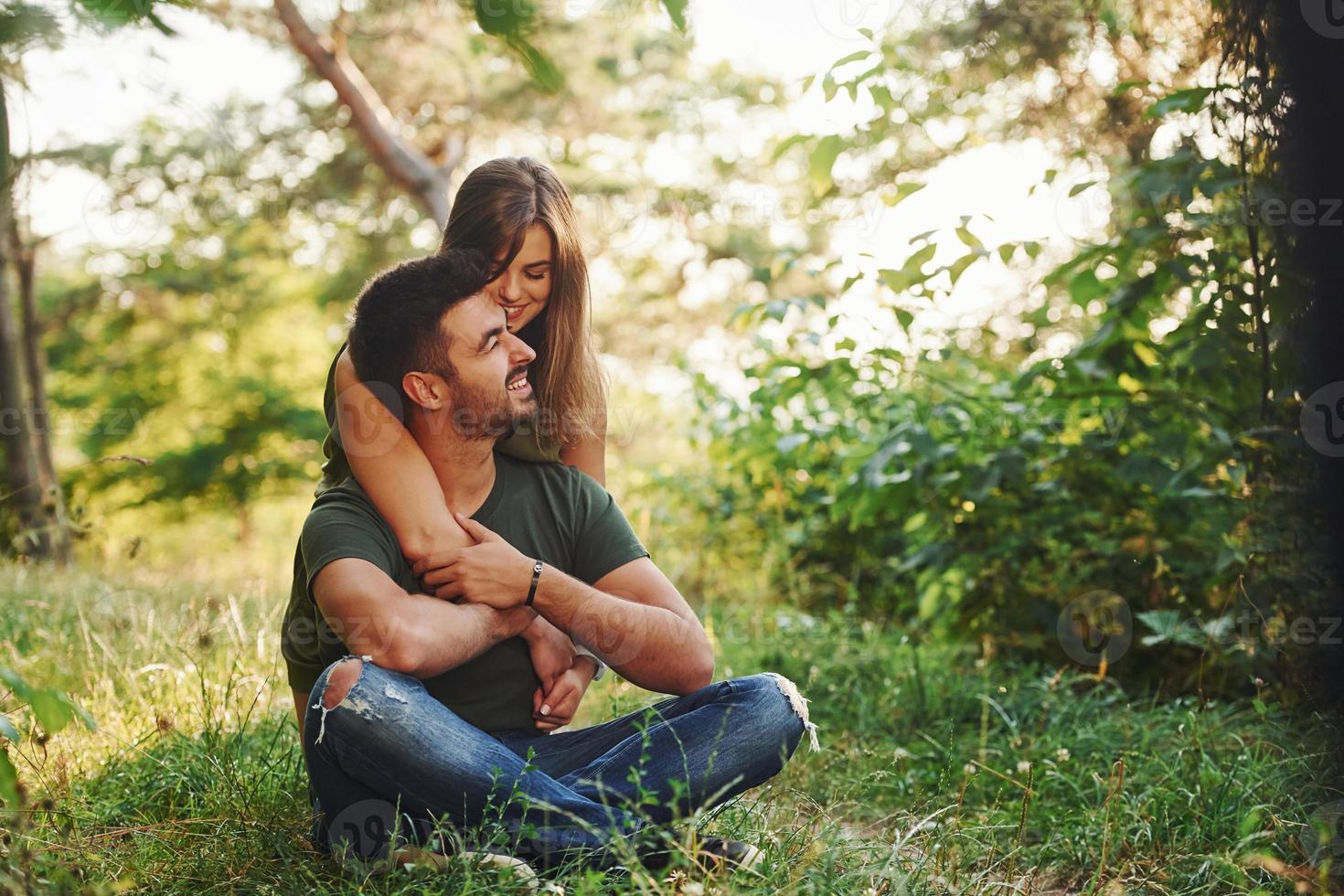 assis et embrassant. beau jeune couple passe un bon moment dans la forêt pendant la journée photo