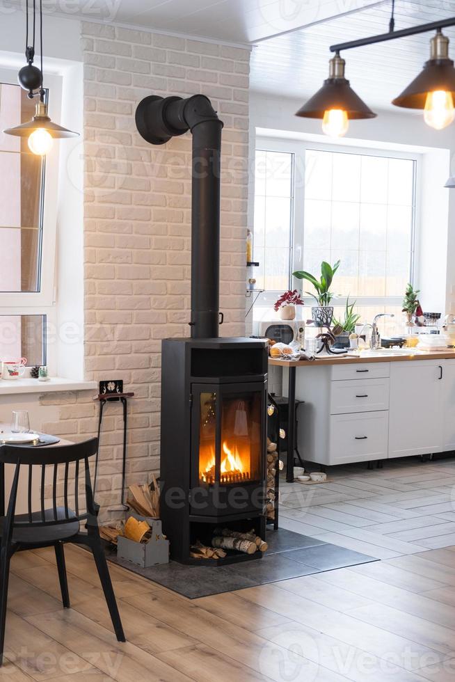 l'intérieur festif de la maison est décoré pour noël et le nouvel an dans un style loft avec poêle noir, cheminée, arbre de noël. studio chaleureux avec cuisine blanche, bois brûlant, cosy et chauffage de la maison photo