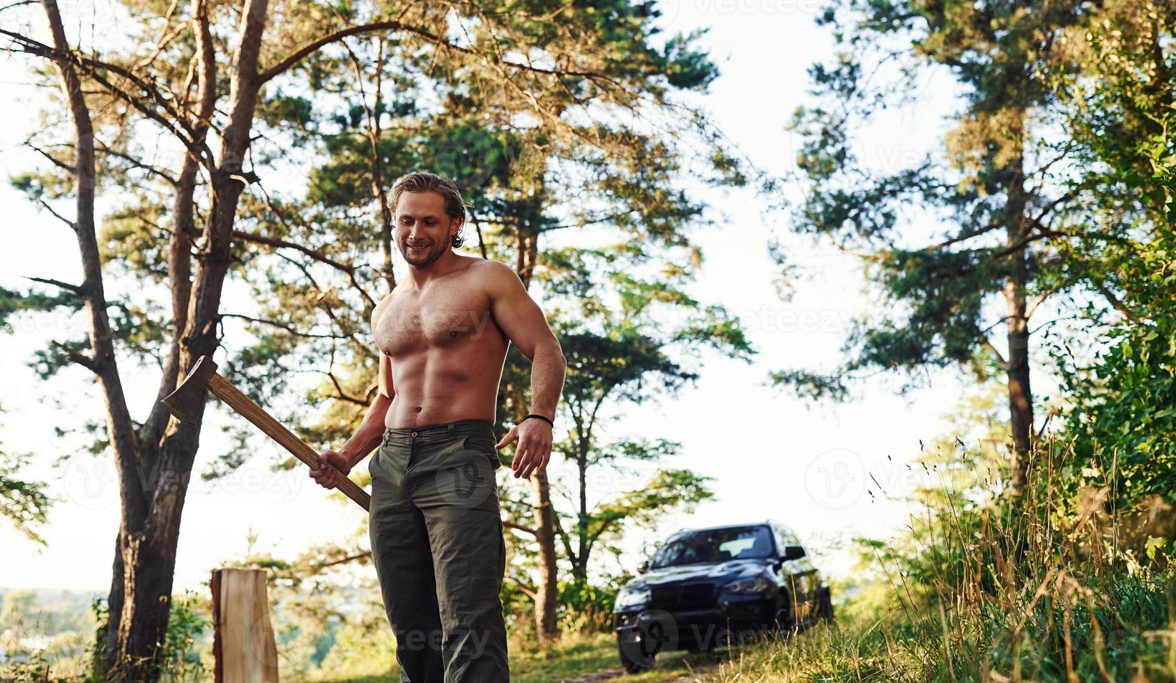 bûcheron avec une hache coupant du bois. bel homme torse nu avec un type de corps musclé est dans la forêt pendant la journée photo