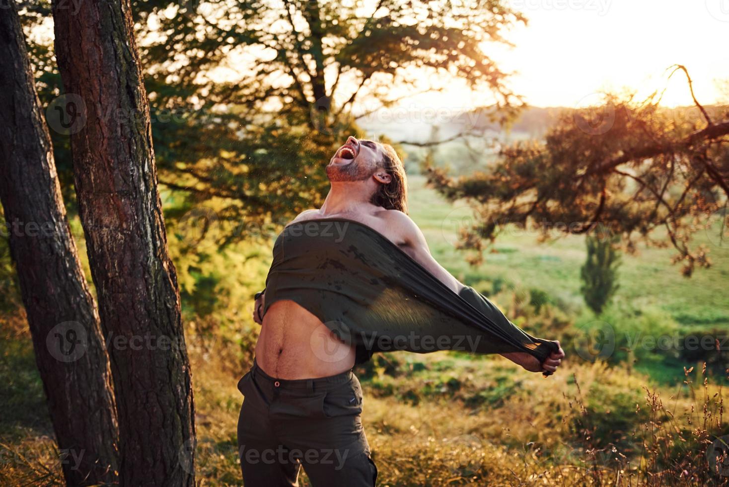 crier et déchirer la chemise. conception de la liberté. bel homme dans la forêt. beau temps. belle lumière du soleil orange photo