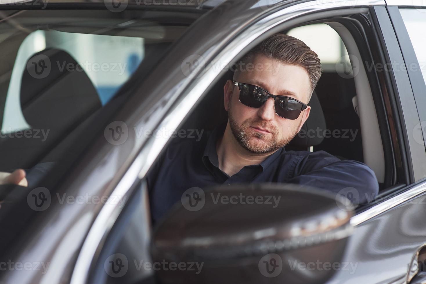 homme d'affaires sérieux en vêtements officiels essayant sa nouvelle voiture dans un salon automobile photo