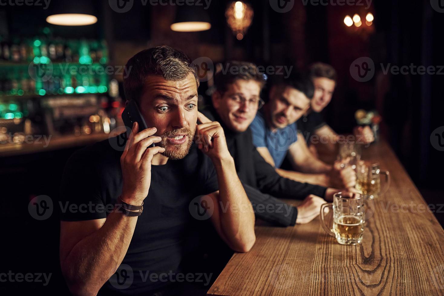 l'homme parle au téléphone. trois fans de sport dans un bar regardent le football. avec de la bière dans les mains photo