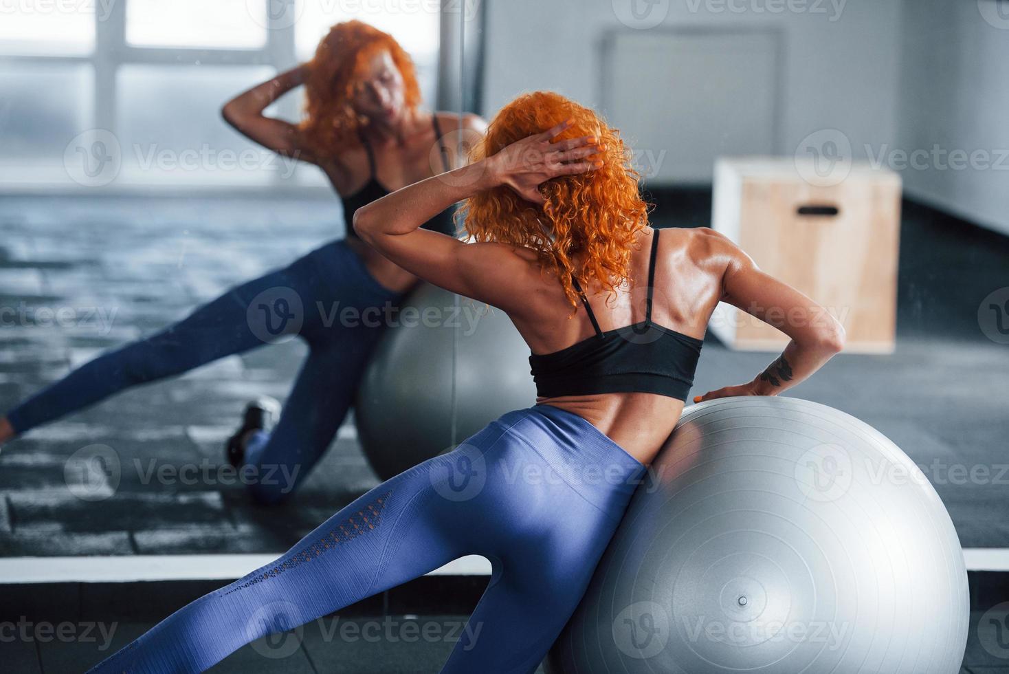 à l'aide d'un ballon d'exercice argenté. une fille rousse sportive a une journée de remise en forme dans la salle de sport pendant la journée. type de corps musclé photo