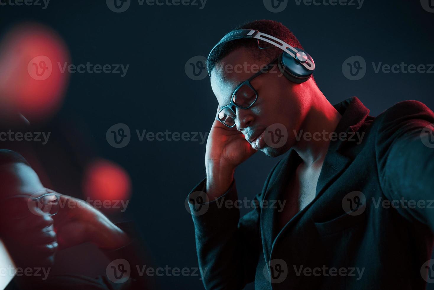 profiter de l'écoute de la musique dans les écouteurs. dans des verres. éclairage néon futuriste. jeune homme afro-américain dans le studio photo