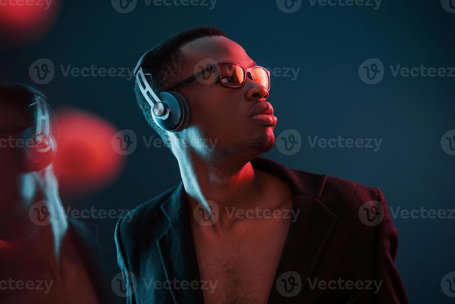 profiter de l'écoute de la musique dans les écouteurs. dans des verres. éclairage néon futuriste. jeune homme afro-américain dans le studio photo