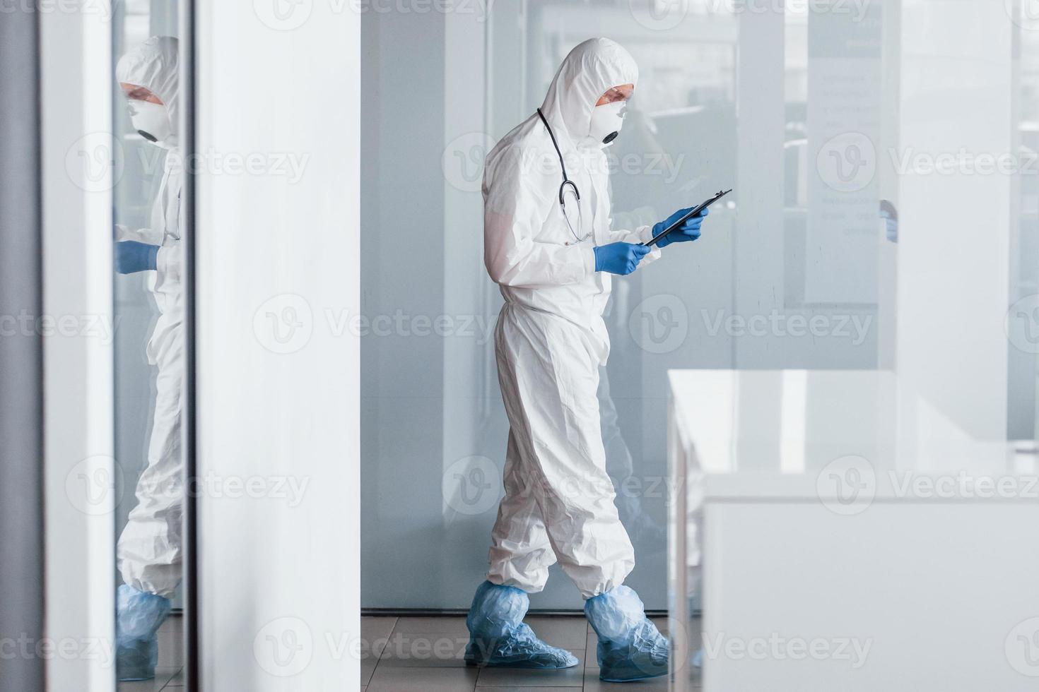 médecin scientifique de sexe masculin en blouse de laboratoire, lunettes défensives et masque tenant le bloc-notes dans les mains photo