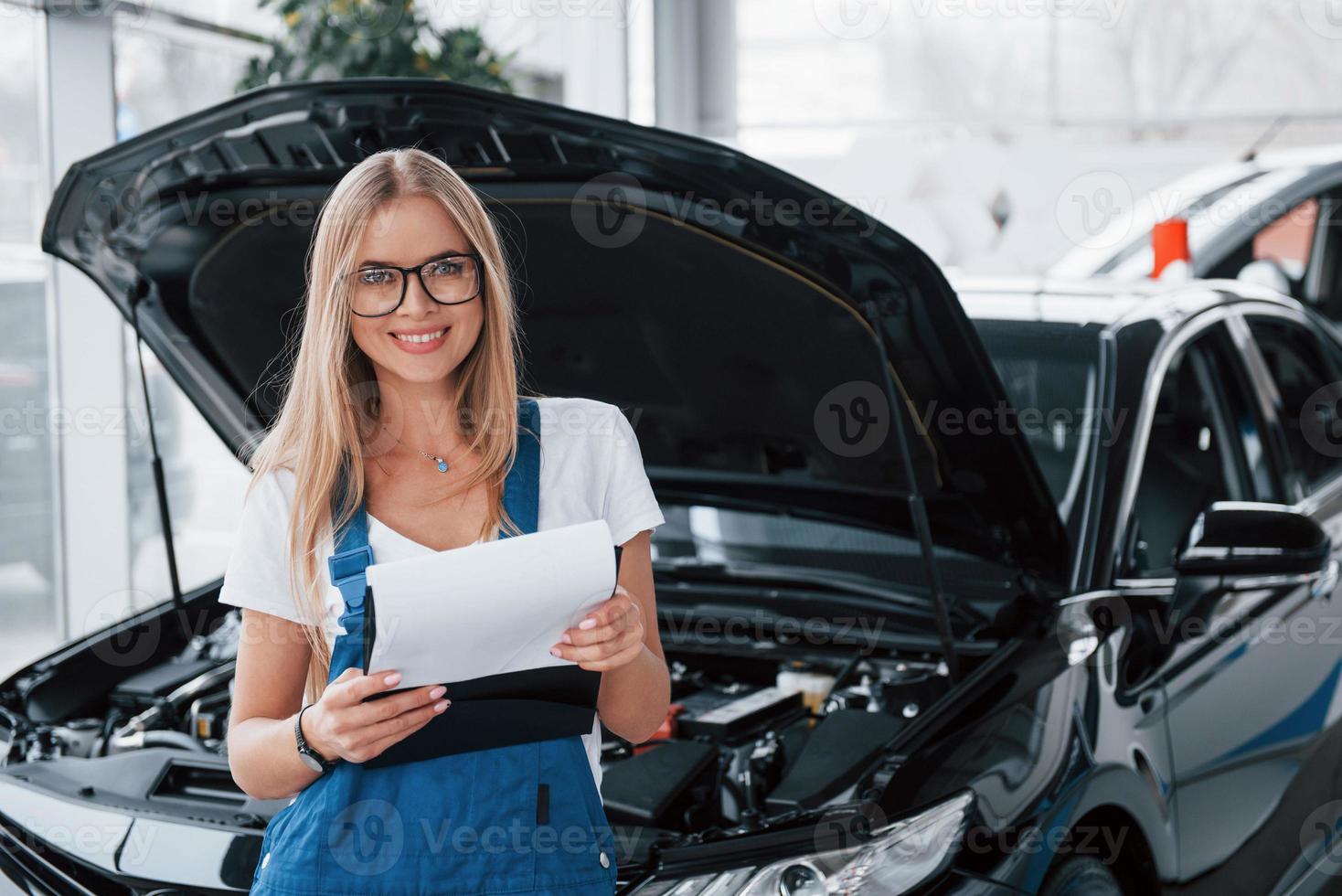 rendre vos véhicules cassés encore plus beaux. gestionnaire avec bloc-notes, dans la chemise blanche et l'uniforme bleu se dresse contre l'automobile avec le capot vers le haut photo