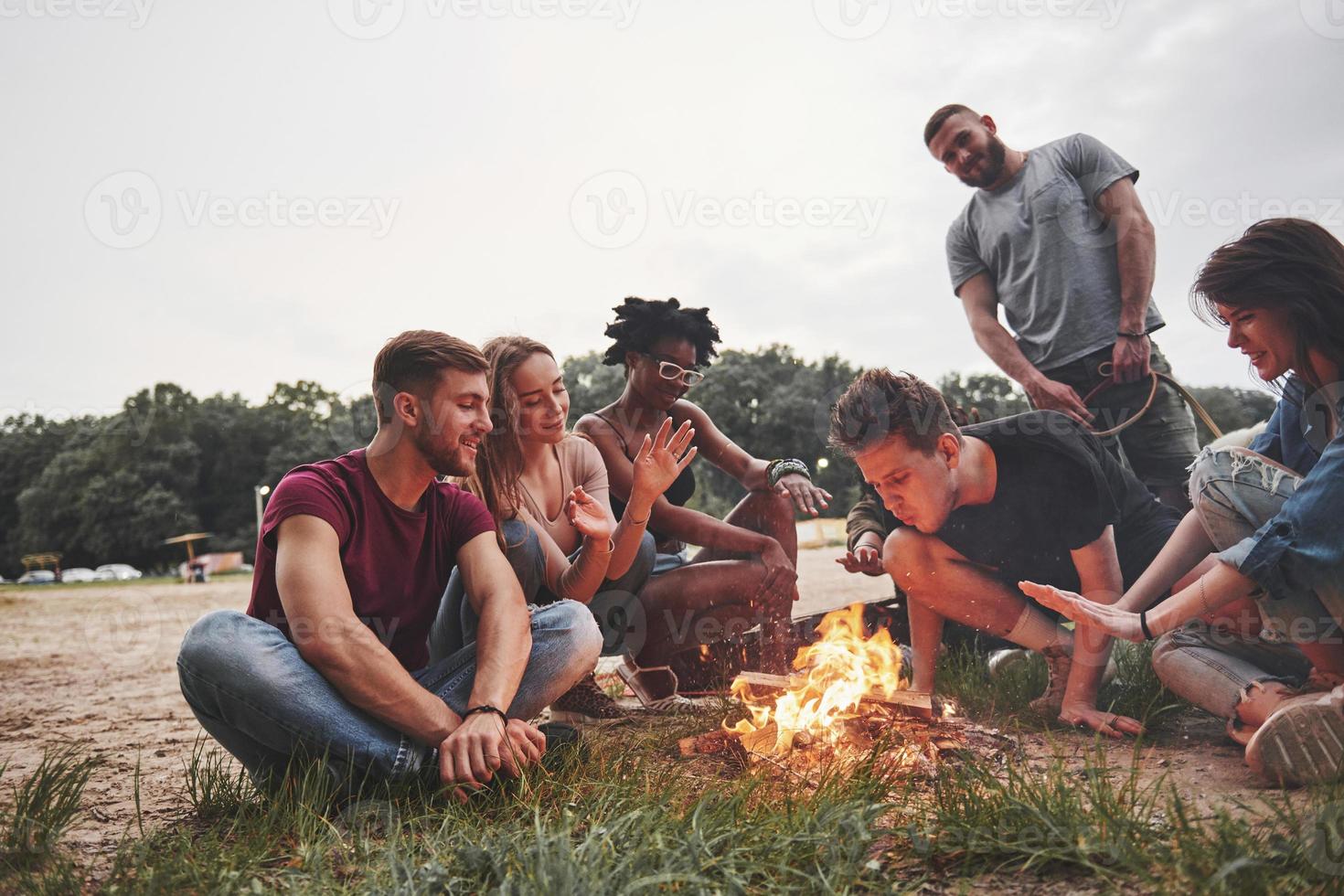 assis autour du feu. groupe de personnes pique-nique sur la plage. les amis s'amusent le week-end photo