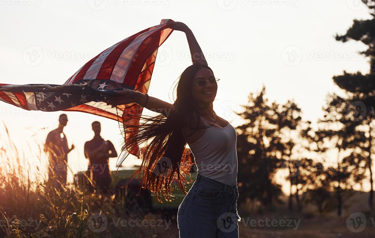 sent la liberté. les amis passent un bon week-end à l'extérieur près de leur voiture verte avec le drapeau américain photo