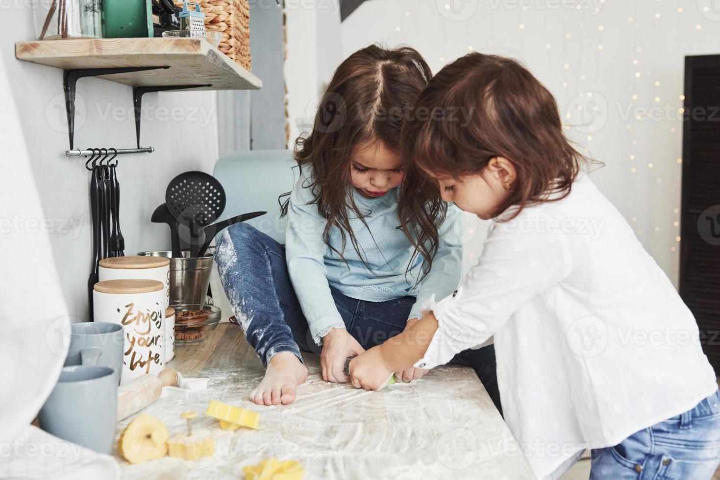 deux petites filles s'amusant. amis d'âge préscolaire apprenant à cuisiner avec de la farine dans la cuisine blanche photo